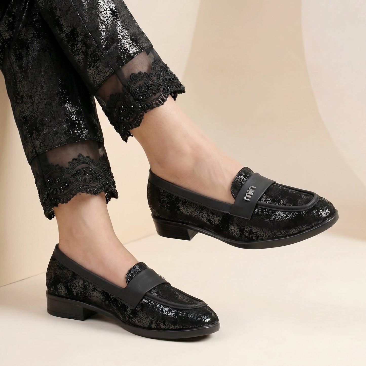 Black sequin loafers worn with black pants on a beige background
