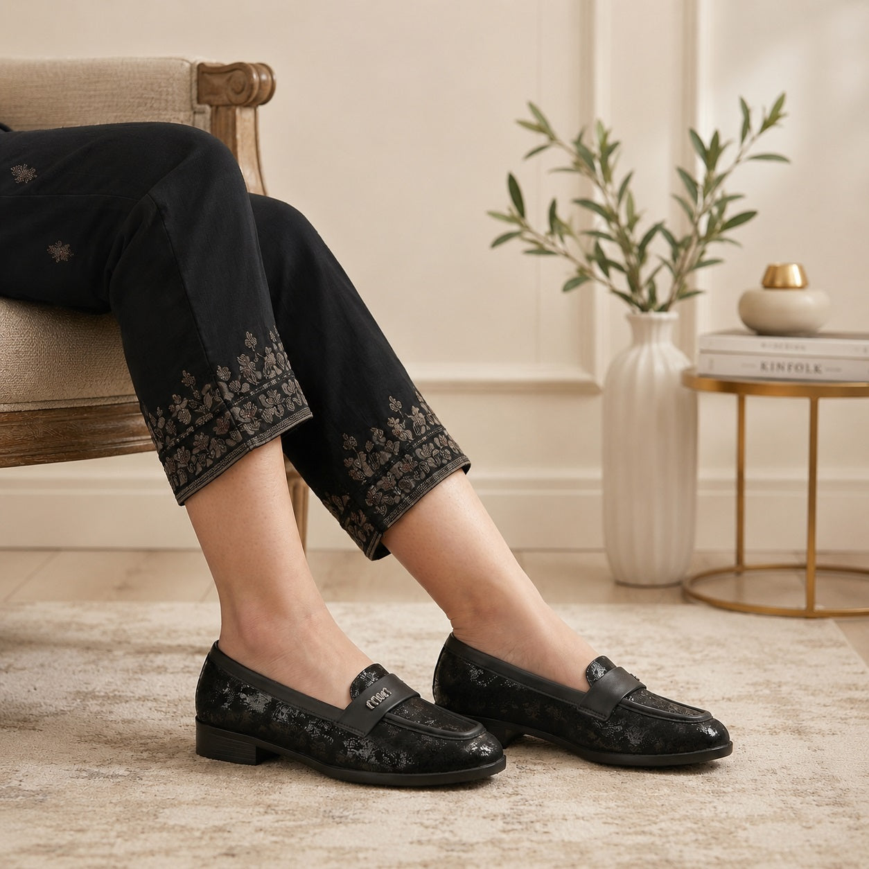 Person wearing black loafers sitting on a chair with a decorative background