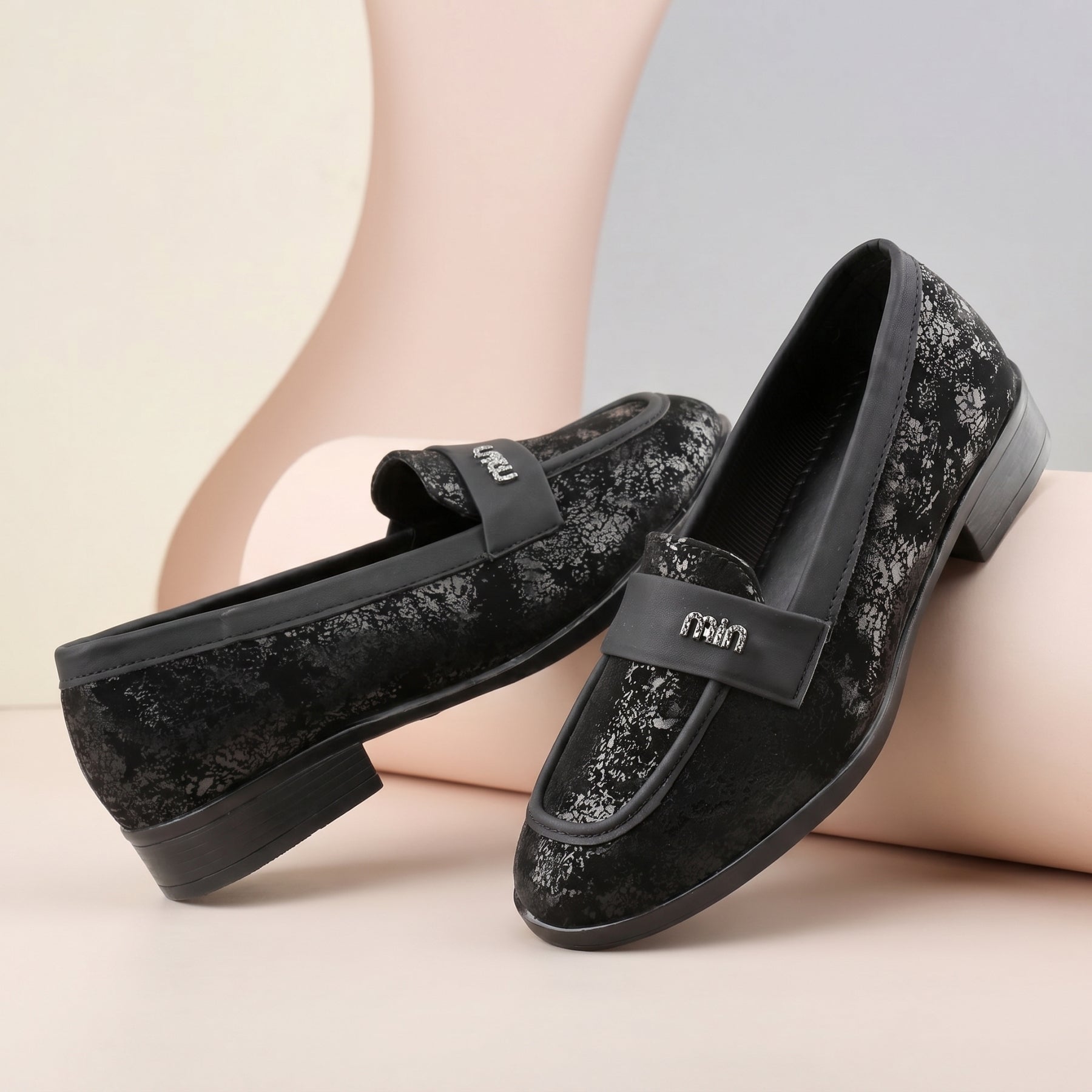 Black glittery loafers with a brand logo on a neutral background
