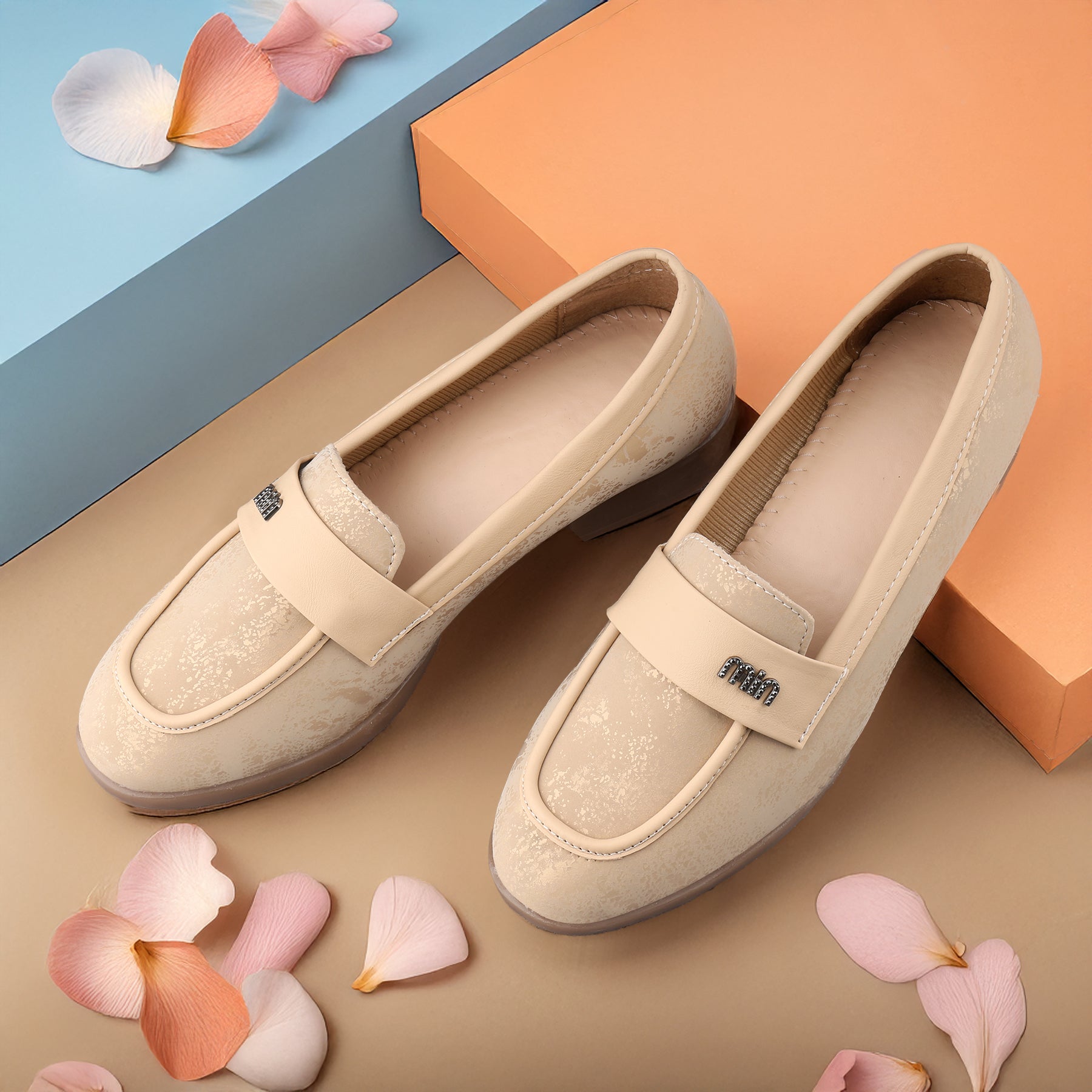 Pair of beige loafers on a colorful background with flower petals