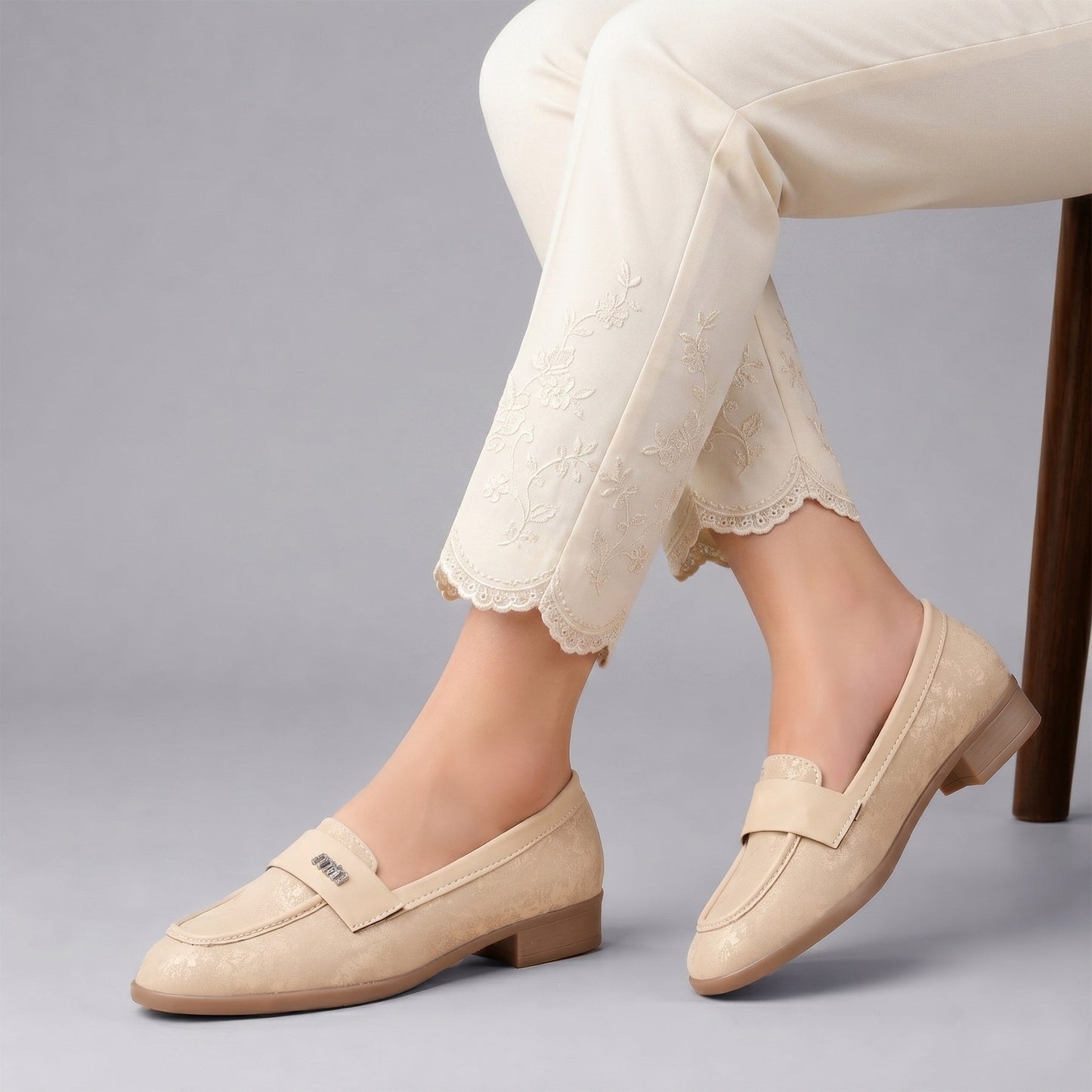 Beige loafers worn with white pants on a gray background