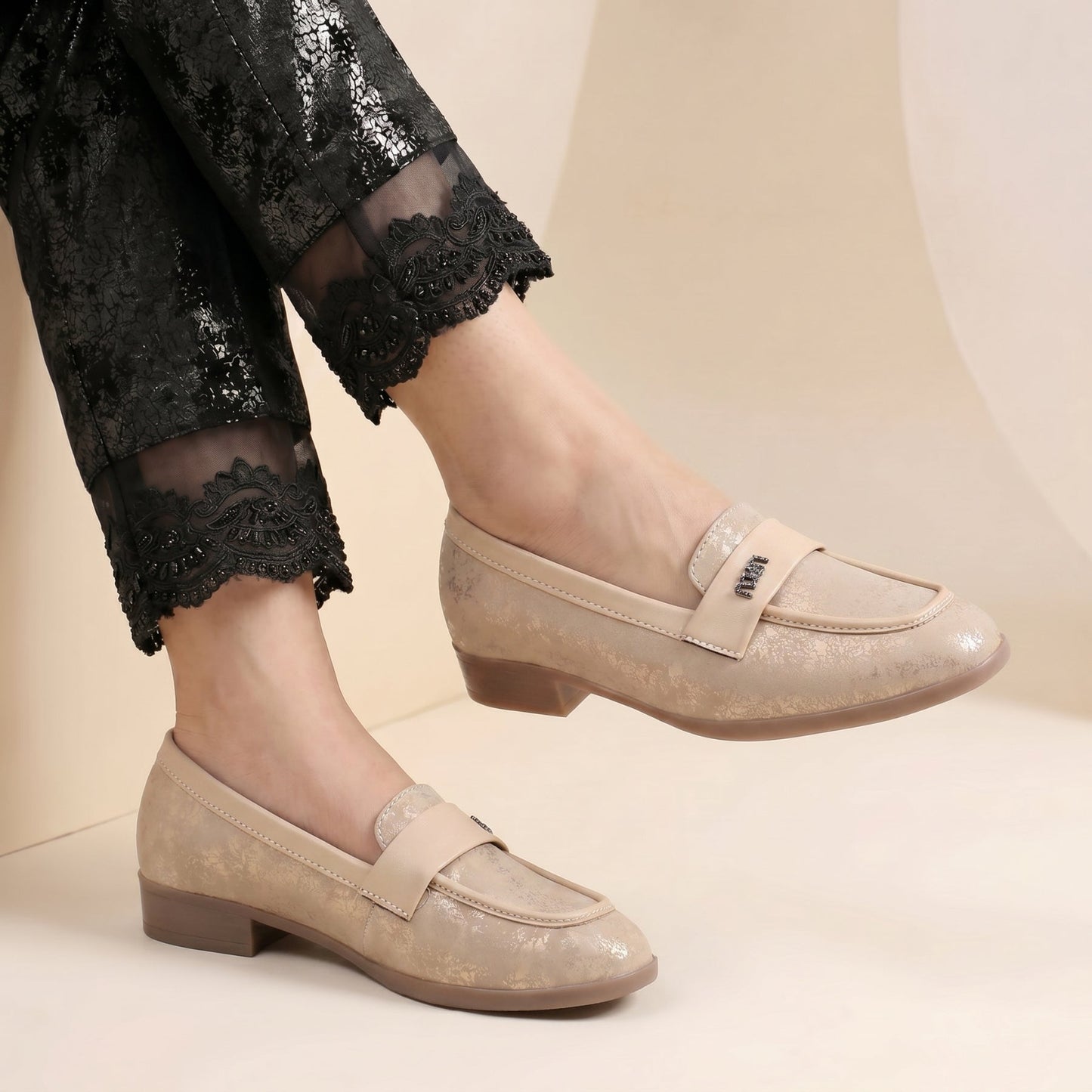 Beige loafers worn with black pants on a neutral background