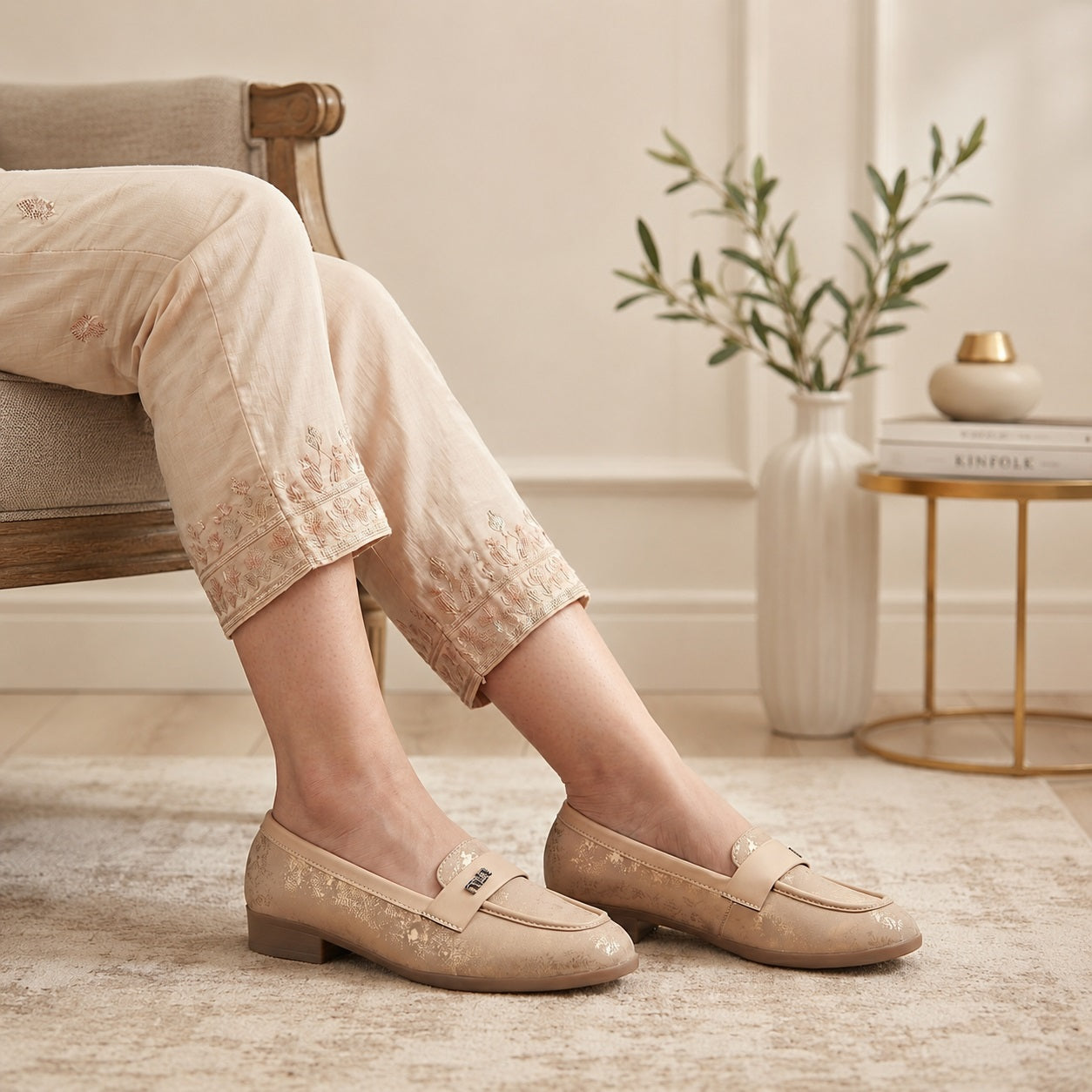 Person wearing beige loafers sitting on a chair with a neutral background