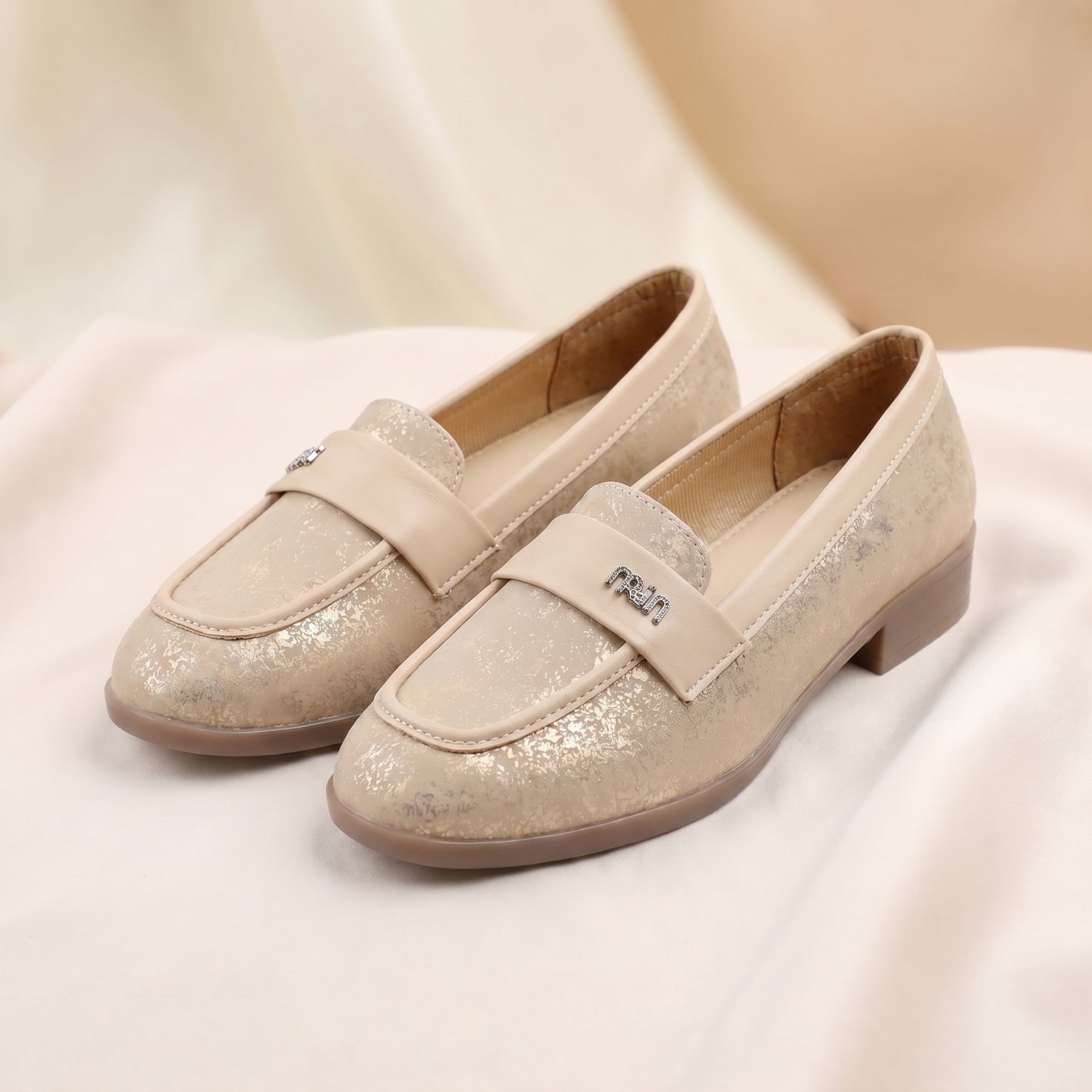 Pair of beige glittery loafers on a soft white background