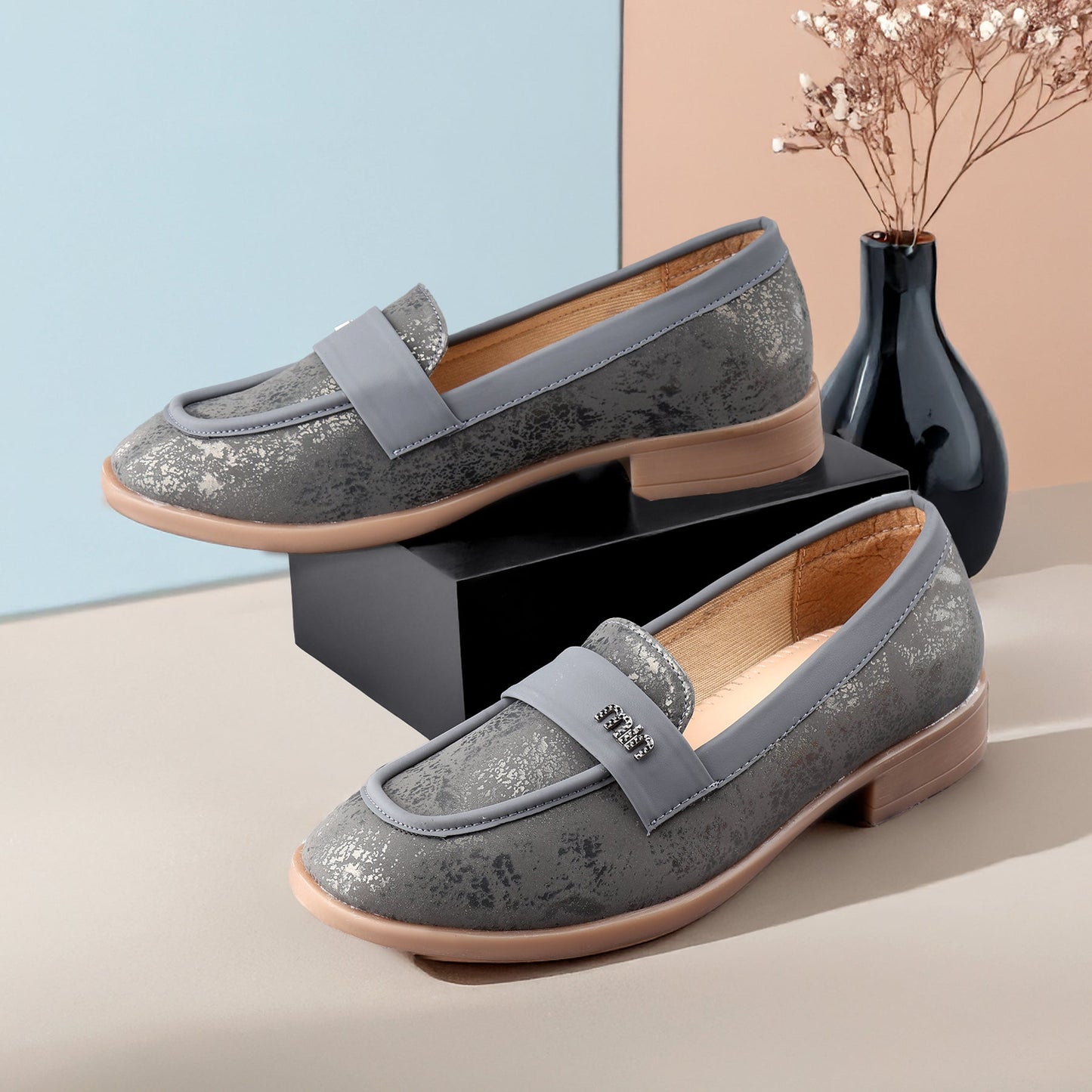 Pair of gray loafers with a decorative bow on a neutral background
