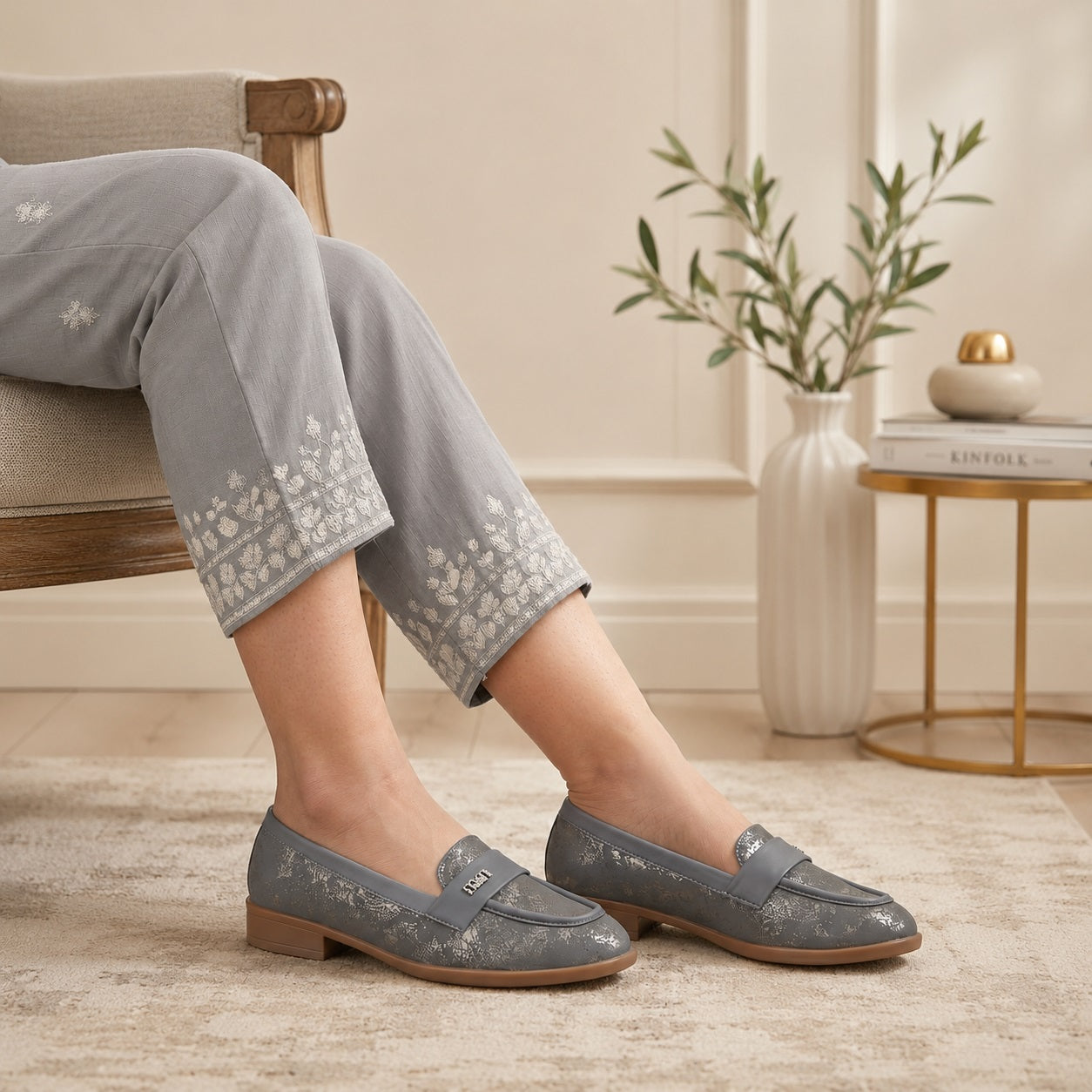 Person wearing gray loafers sitting on a chair with a neutral background