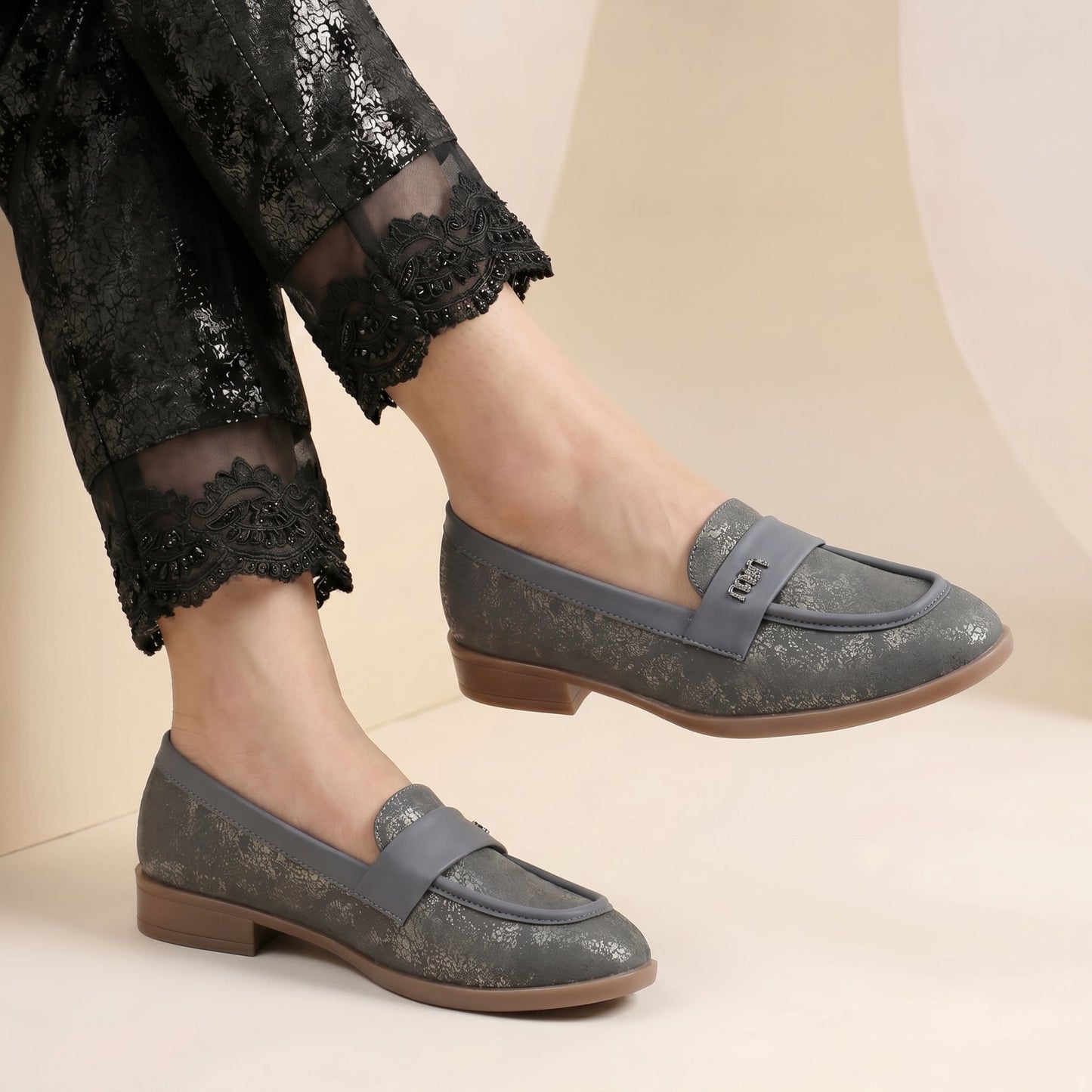Gray loafers worn with black pants on a beige background