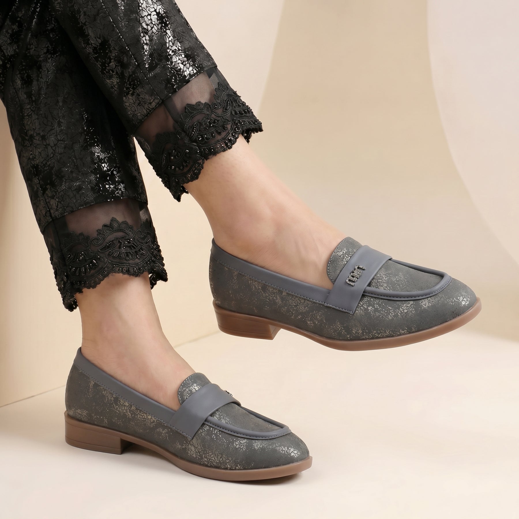 Gray loafers worn with black pants on a beige background