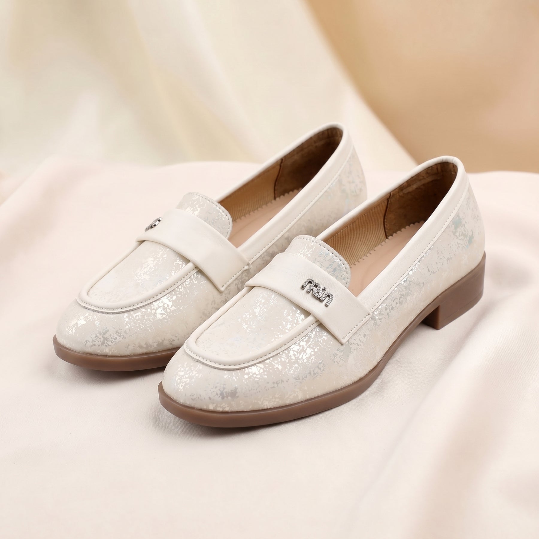 White glittery loafers on a soft beige background