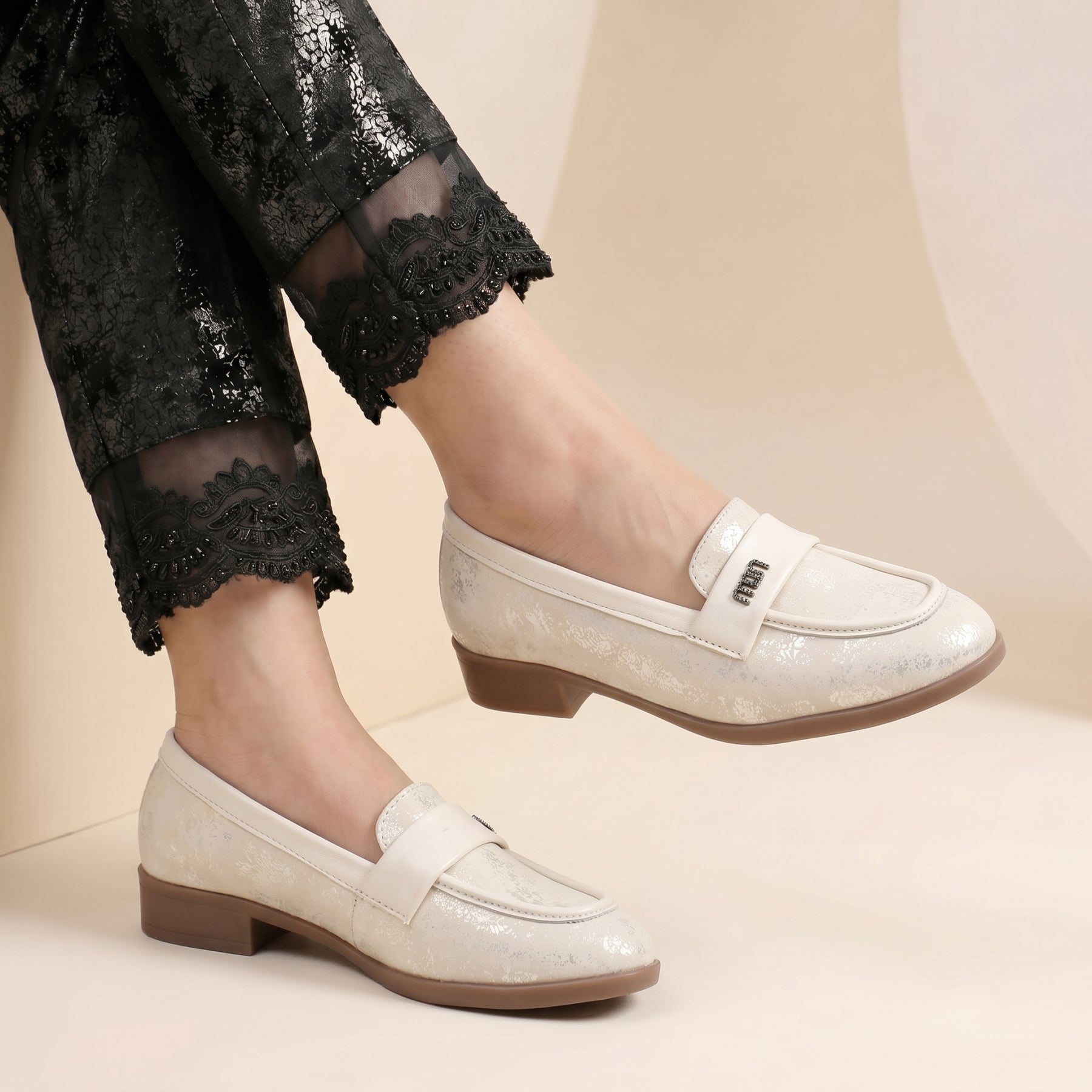 White loafers worn with black pants on a beige background