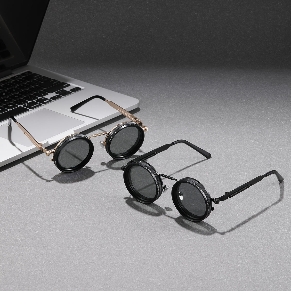 Round sunglasses with gold frames on a gray surface next to a laptop.