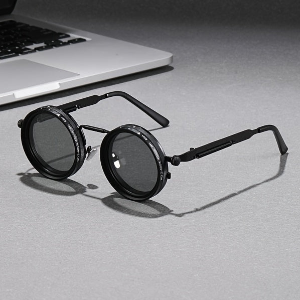 Round sunglasses with dark lenses on a gray surface next to a laptop.