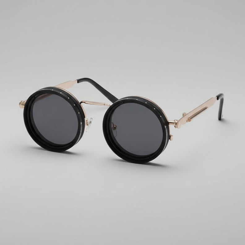Round black sunglasses with gold metal frames and temples, resting on a modern white platform in a minimalist interior setting.