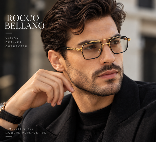 A man wearing Rocco Bellano gold-framed eyeglasses with a black temple and clear lenses, styled with a black coat and turtleneck. The image features text overlays reading 'ROCCO BELLANO' and 'VISION DEFINES CHARACTER' on a blurred urban background.