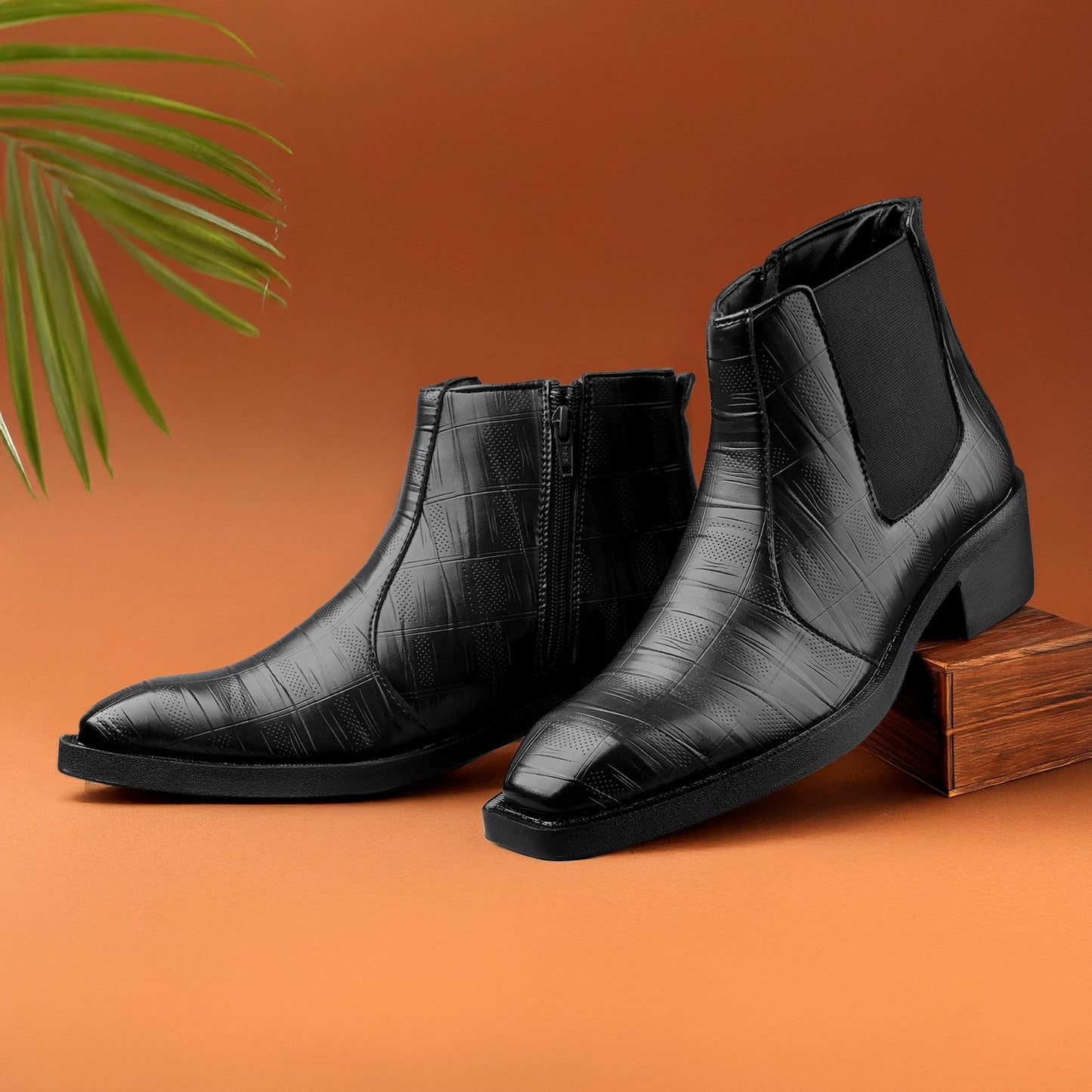 Black leather boots on an orange background with a green leaf.