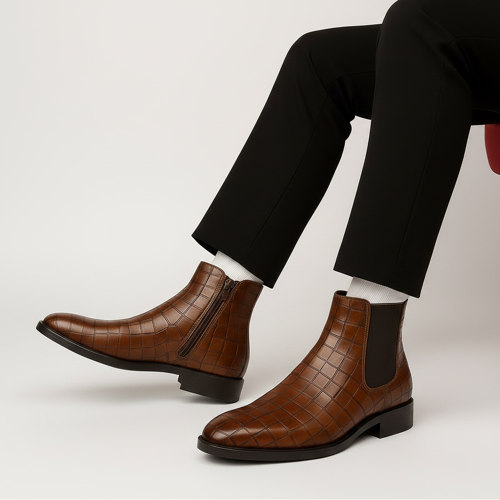 Brown leather Chelsea boots worn with black pants and white socks on a wooden floor.