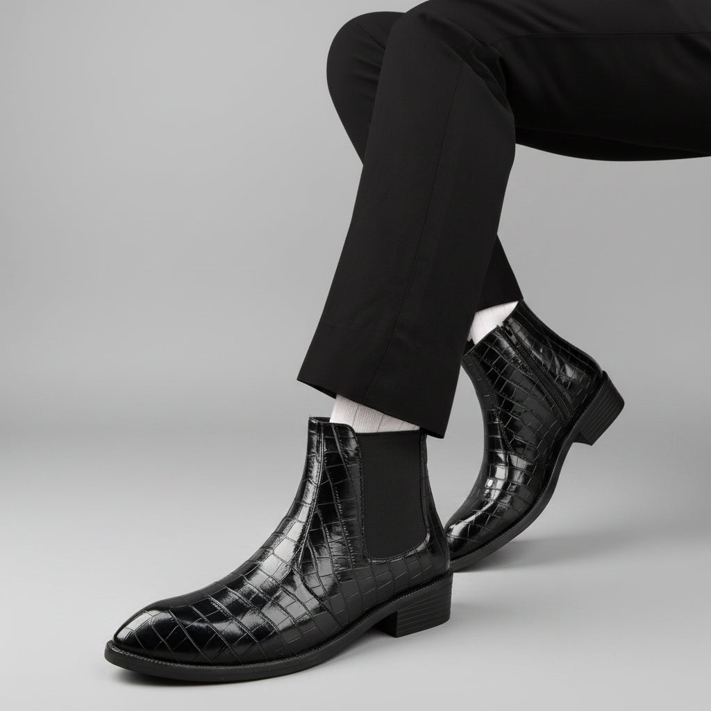 Black crocodile-patterned boots worn with a black suit on a wooden floor.