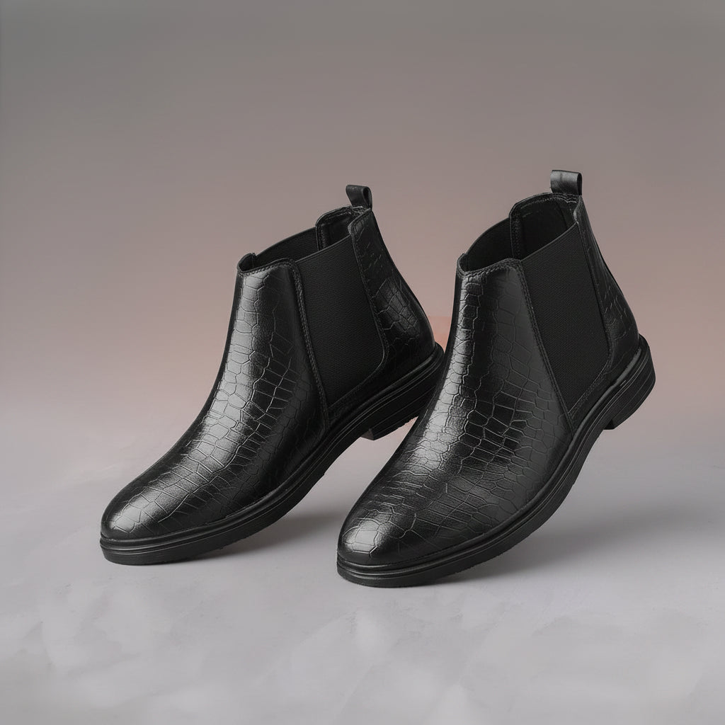 Black leather Chelsea boots on a gray surface with a beige box in the background.