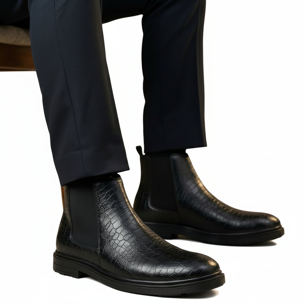 Black crocodile-patterned leather boots worn with dark pants on a neutral background