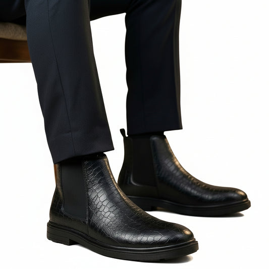 Black crocodile-patterned leather boots worn with dark pants on a neutral background