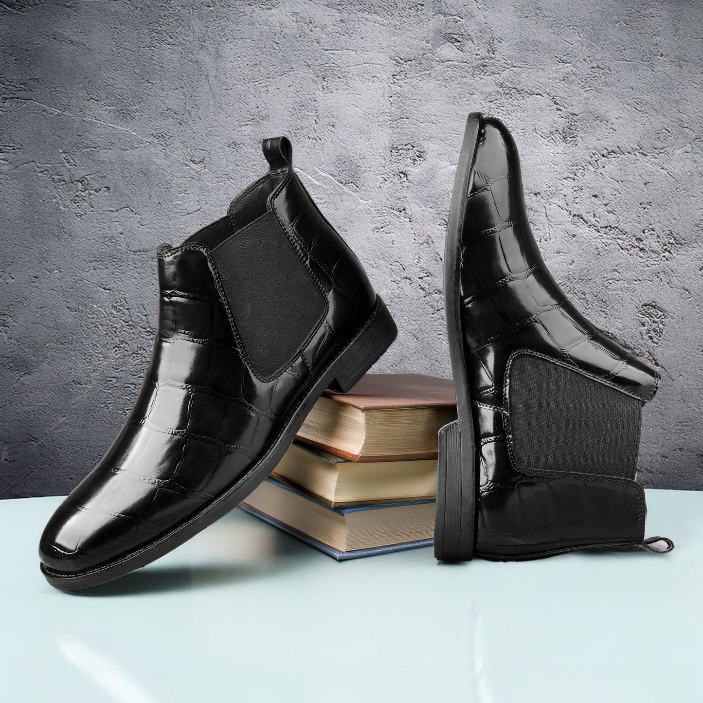 Black patent leather boots on a light blue surface with books underneath, against a gray textured background.