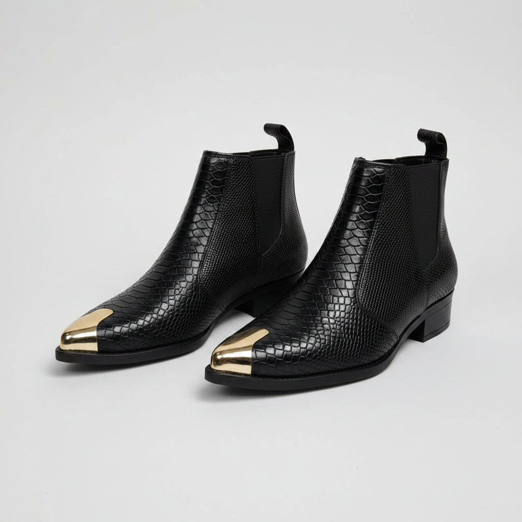 Black ankle boots with gold toes held by a hand, against a Ted Baker background.