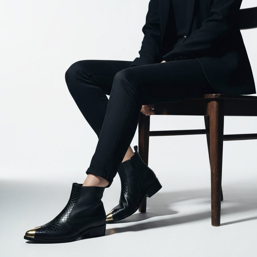 Black ankle boots with gold toe cap on a light gray background
