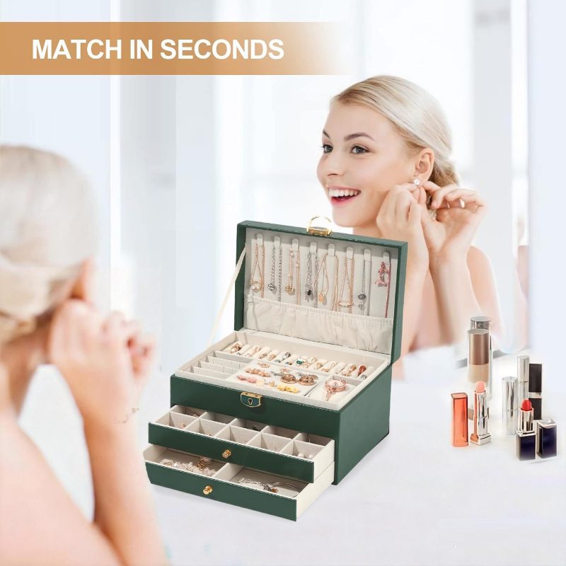 A woman in a bathroom looks at her reflection while wearing earrings, with an open green jewelry box displayed in front of her. The box has multiple compartments and drawers, filled with jewelry.