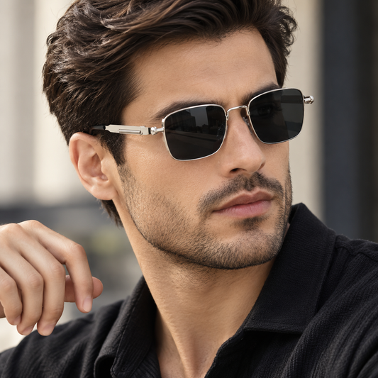 A close-up of a man wearing silver-framed square aviator sunglasses with dark lenses, paired with a black collared shirt.