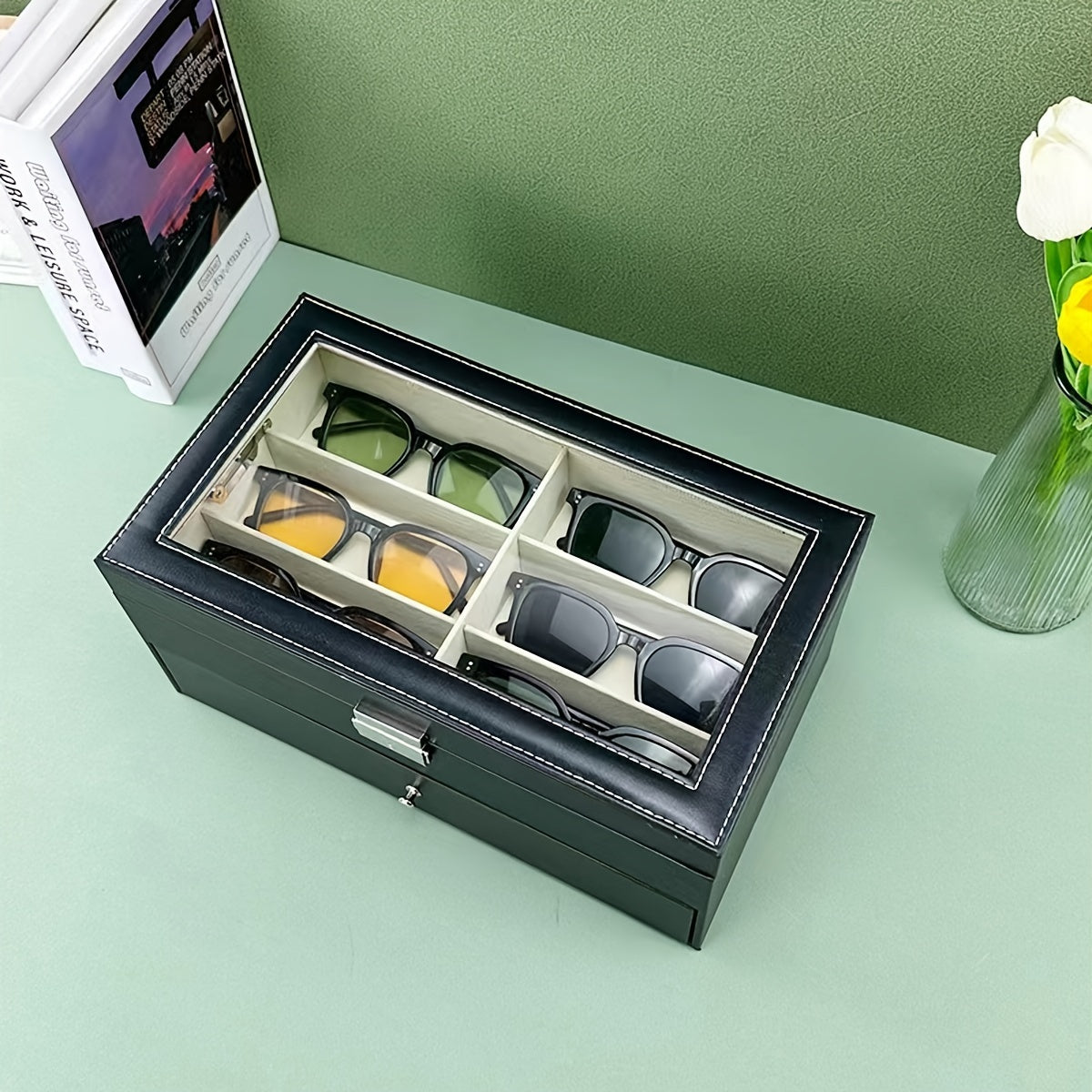 Black glasses case with compartments containing various pairs of eyeglasses on a light green surface.