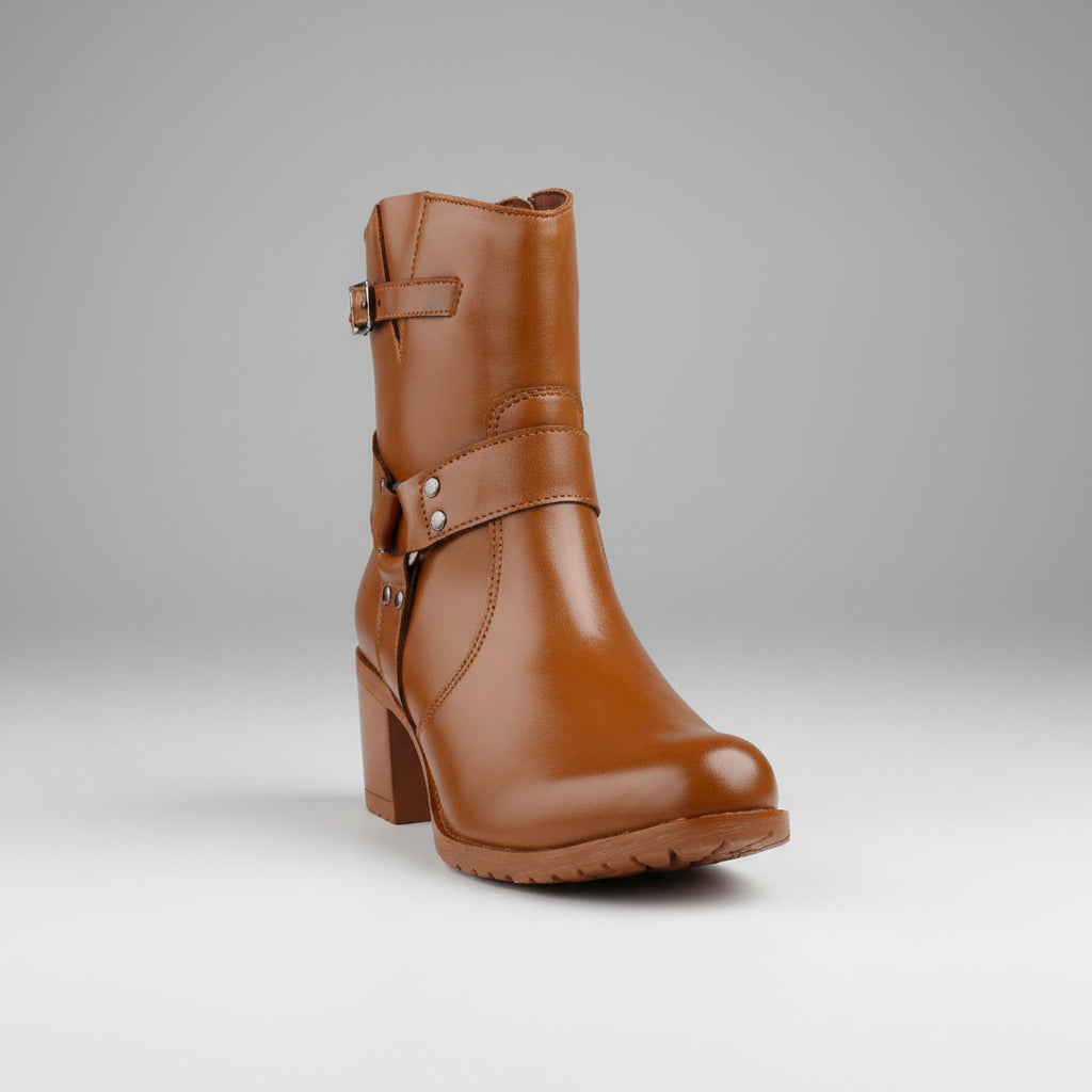 A brown leather ankle boot with a block heel, side buckle strap, and decorative rivet details, displayed on a beige platform against a split pastel background.