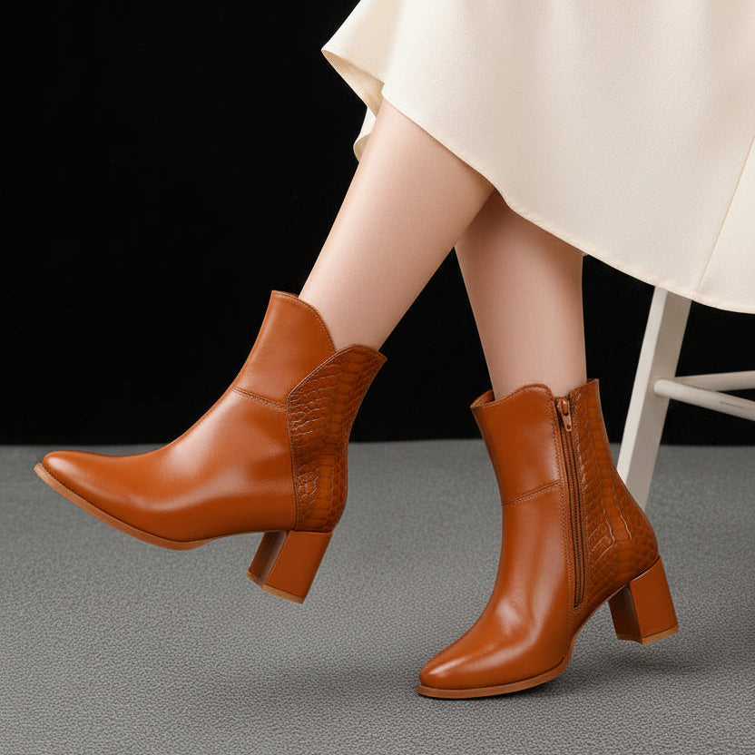 A pair of women's brown leather ankle boots with a block heel and side zipper, shown on a model's feet against a neutral indoor background.
