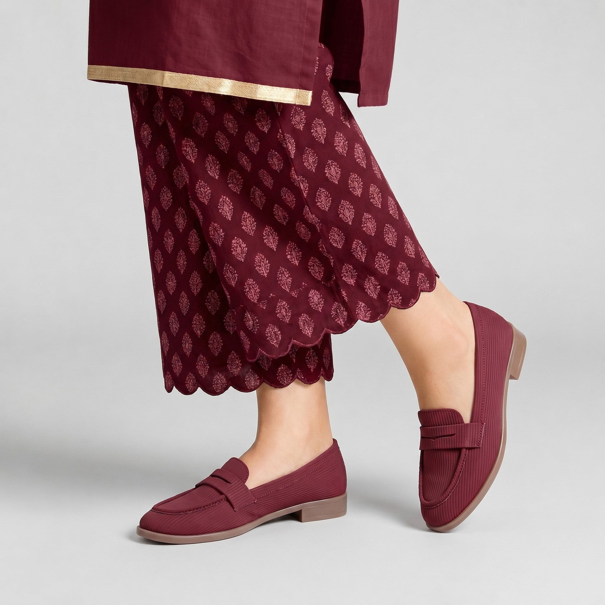 Maroon loafers worn with a matching outfit on a light gray background