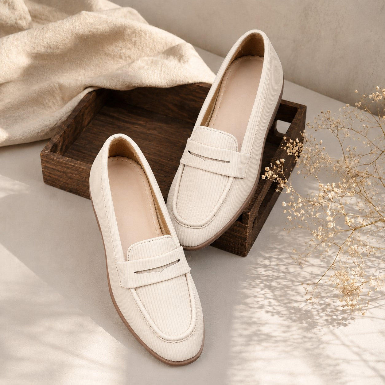 Pair of beige loafers on a wooden tray with a neutral background