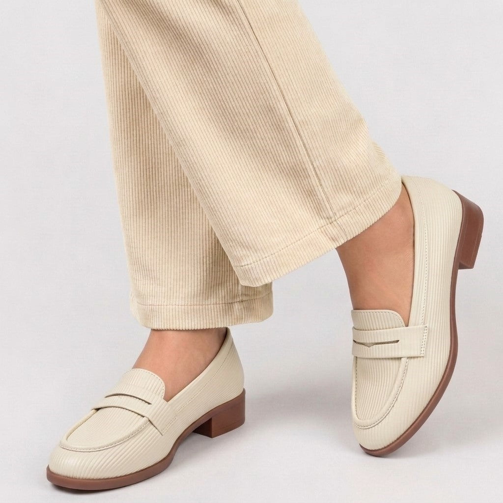Beige loafers worn with beige pants on a light gray background