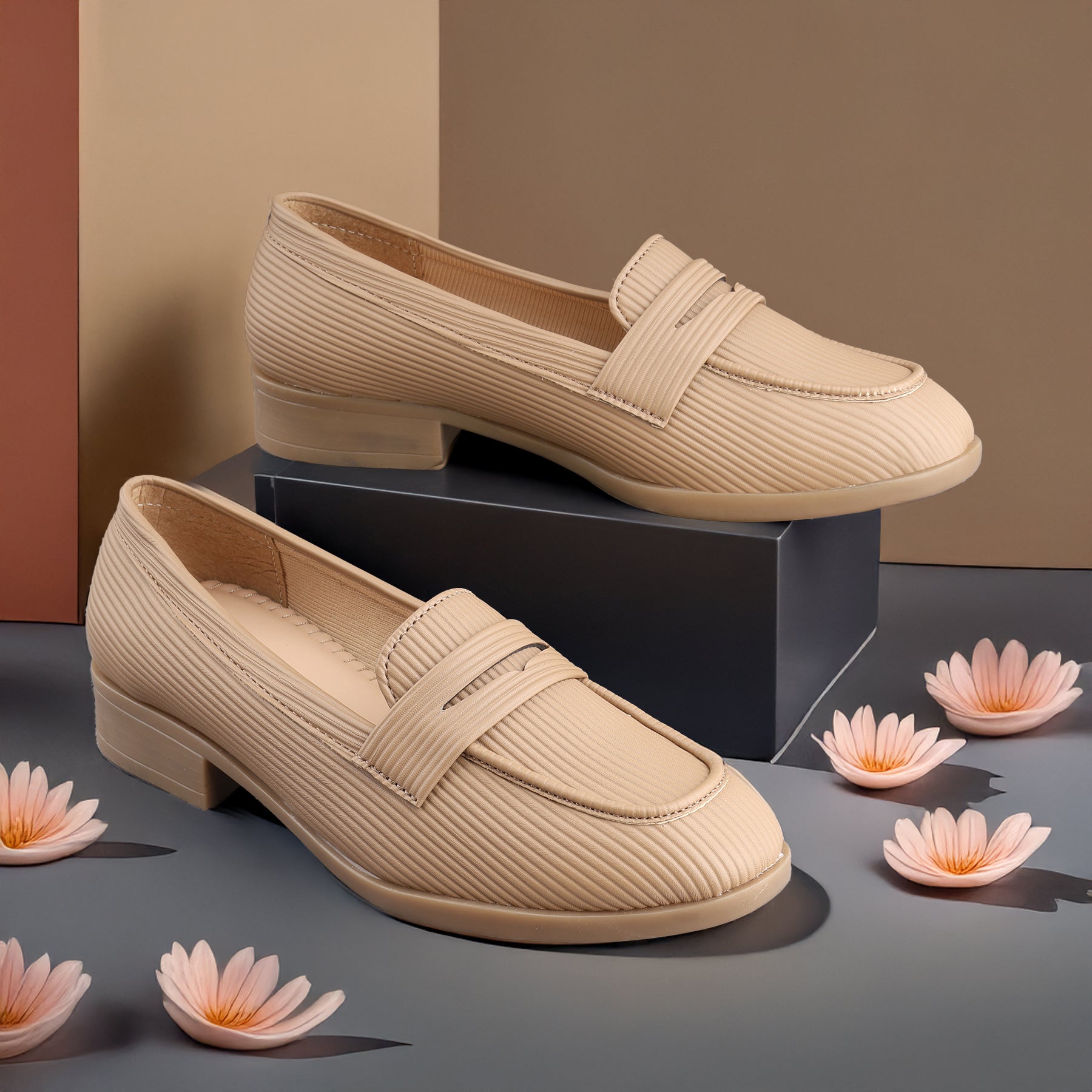 Beige loafers on a dark surface with pink flowers around them
