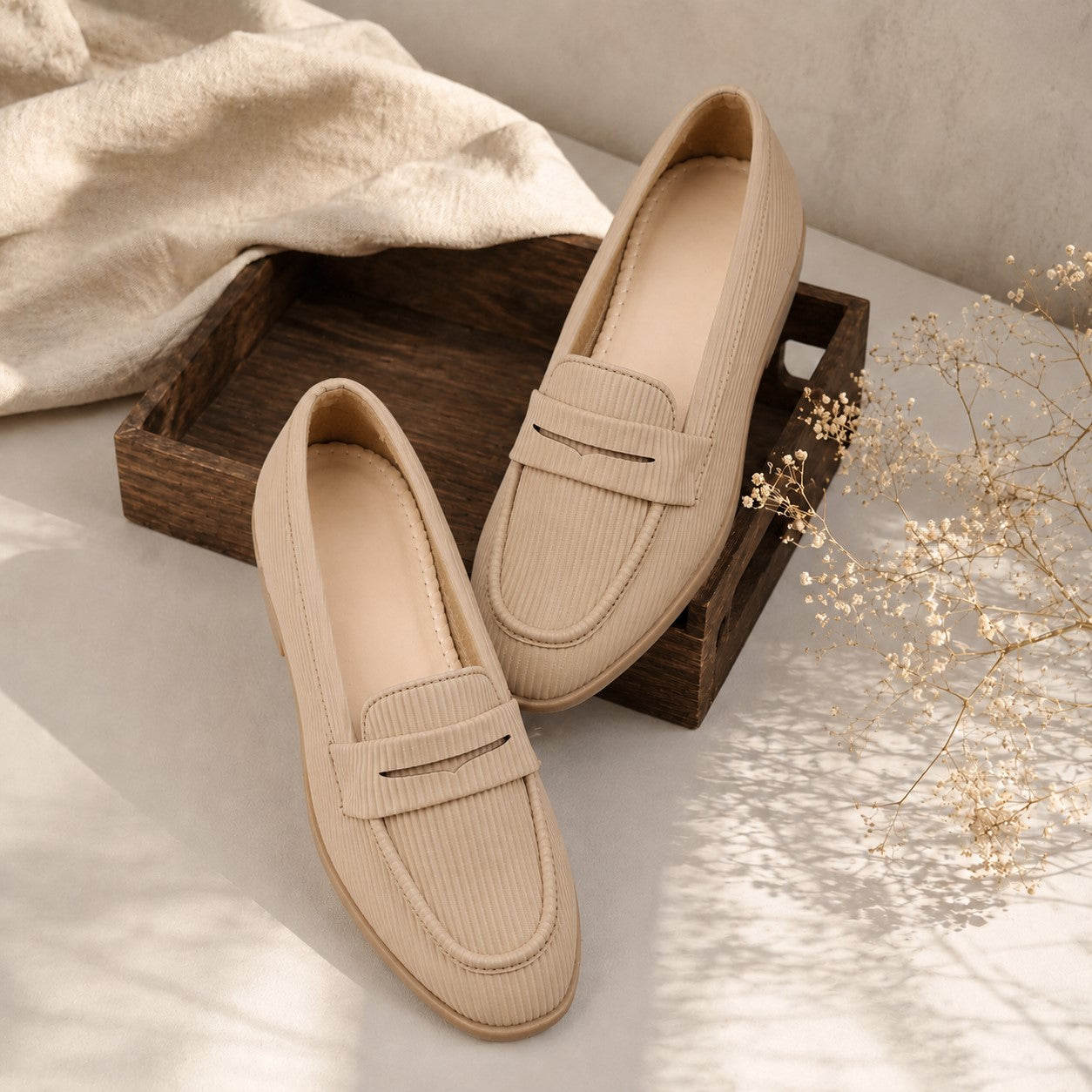 Pair of beige loafers on a wooden tray with a neutral background