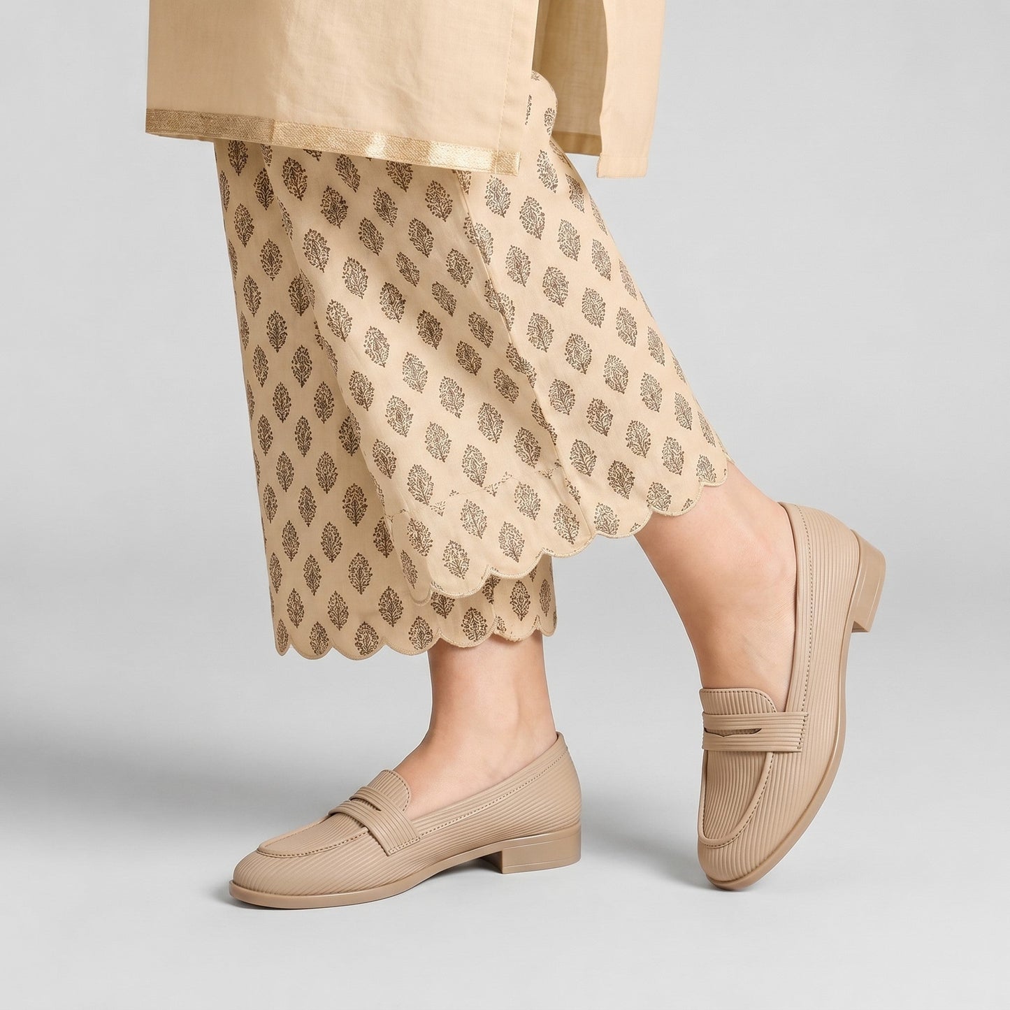 Person wearing beige loafers and a patterned skirt on a light gray background