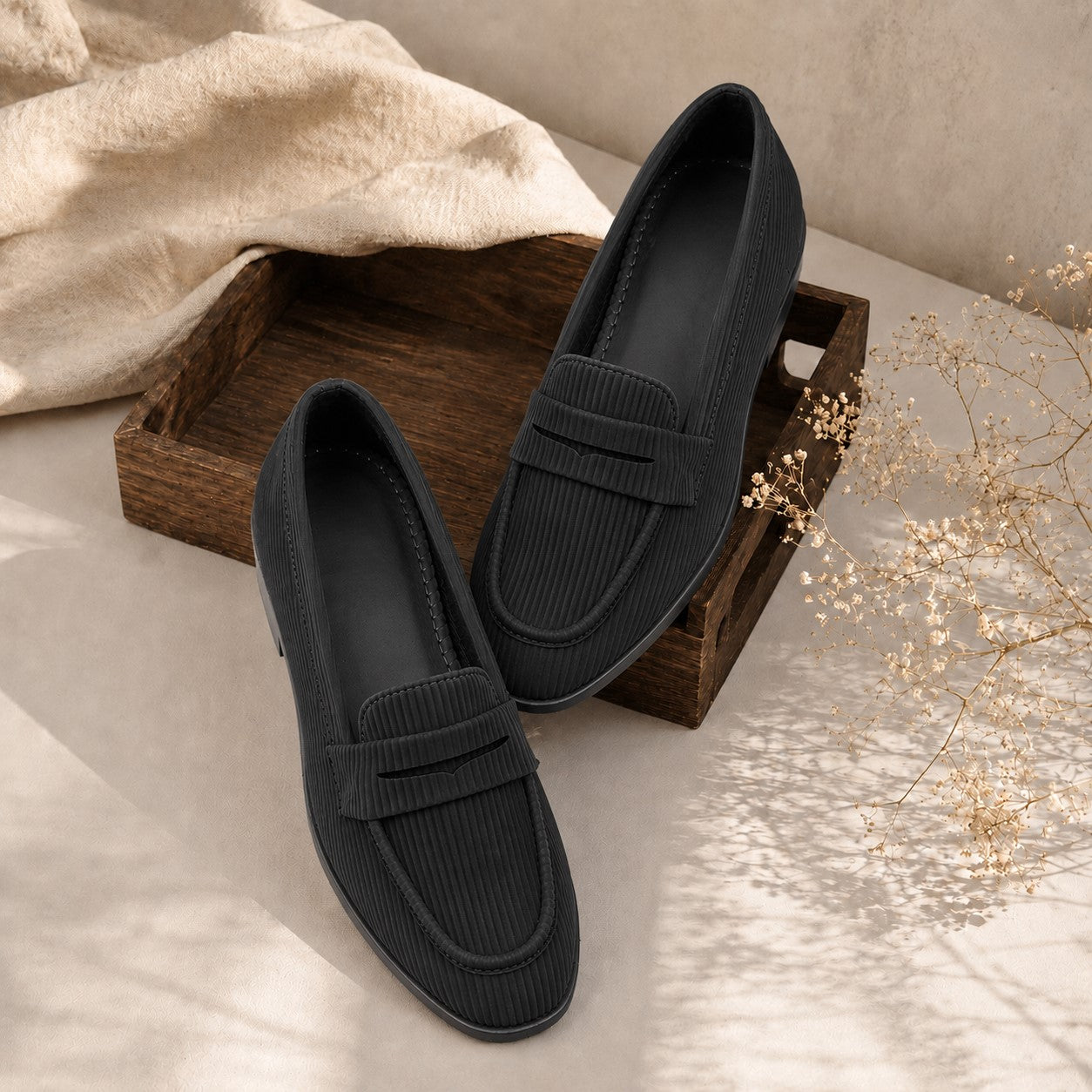Pair of black loafers on a wooden tray with a neutral background