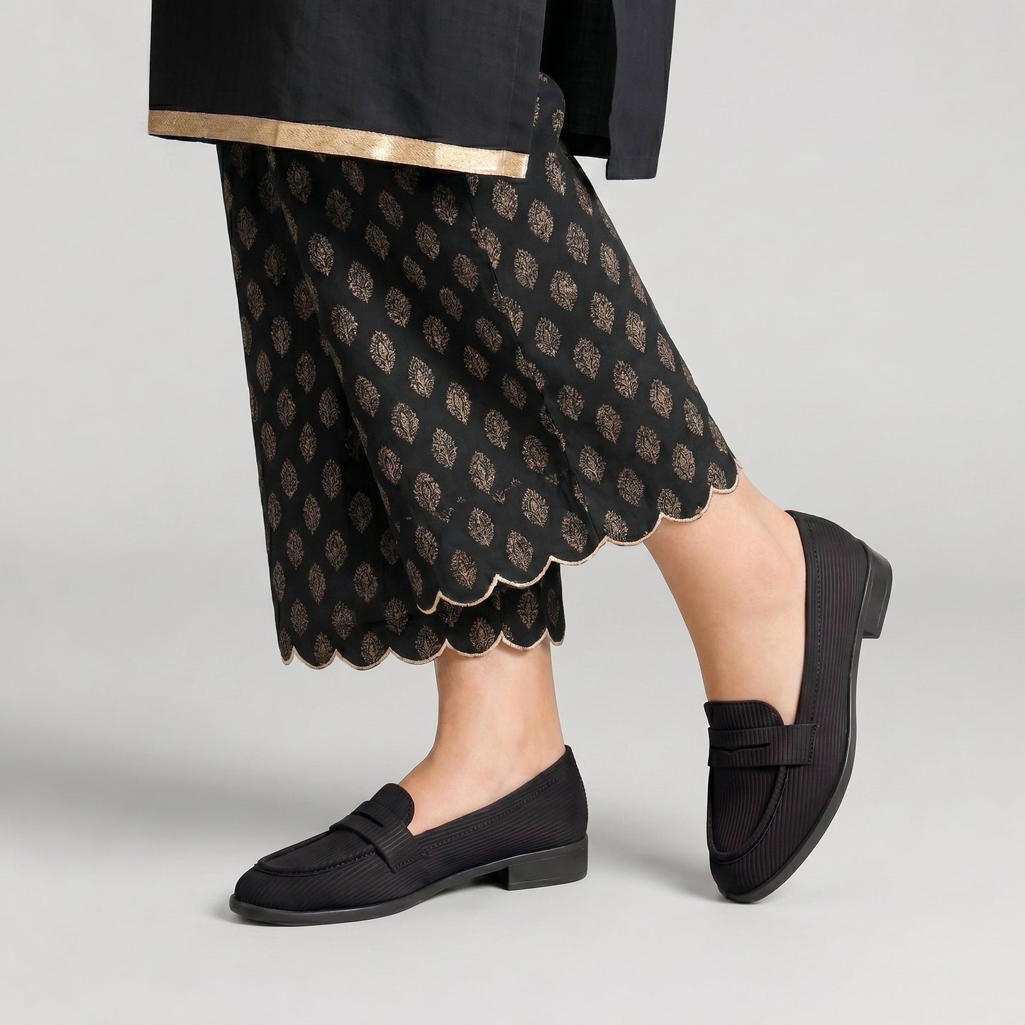 Person wearing black loafers and a patterned black skirt on a light gray background