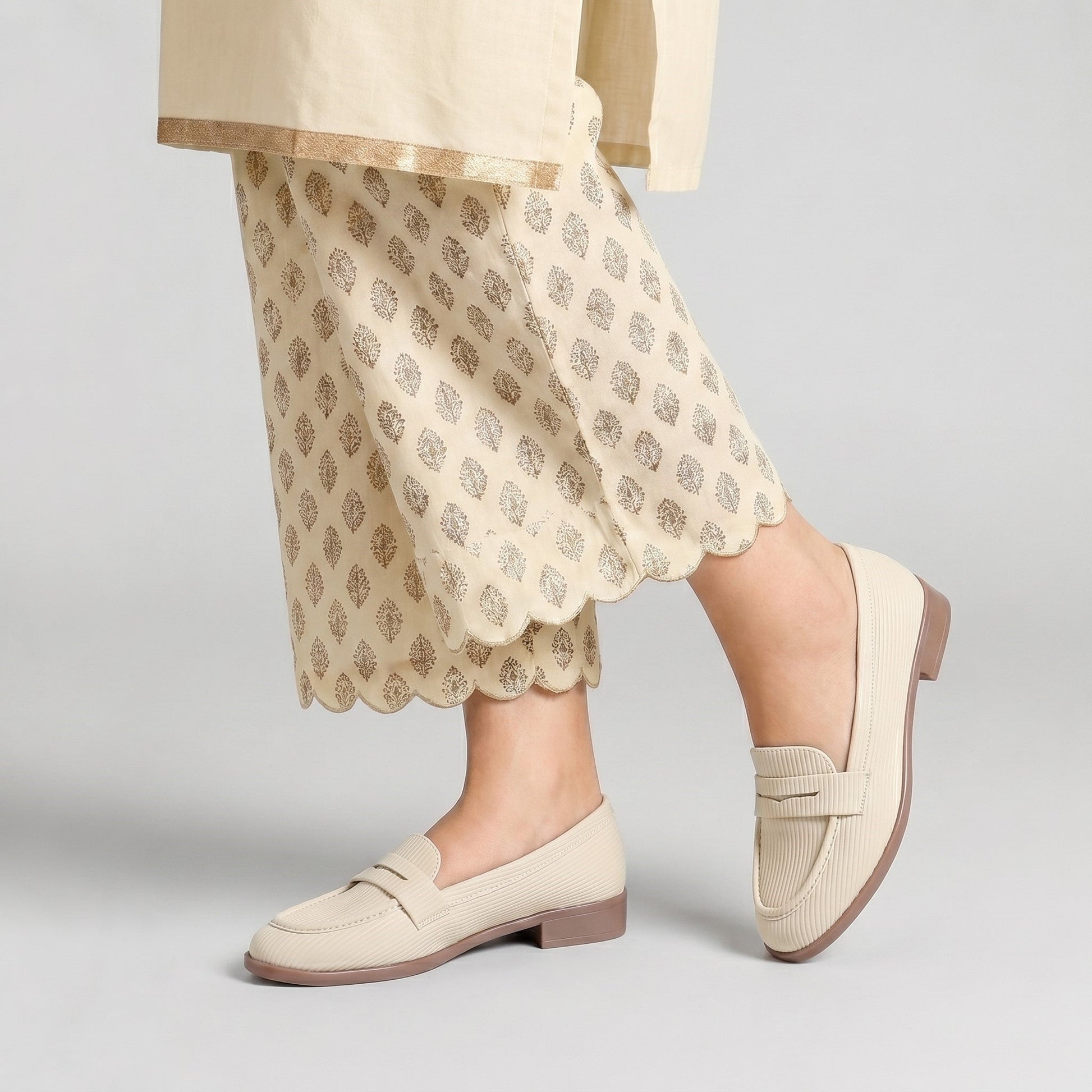 Beige loafers worn with a patterned skirt on a light gray background