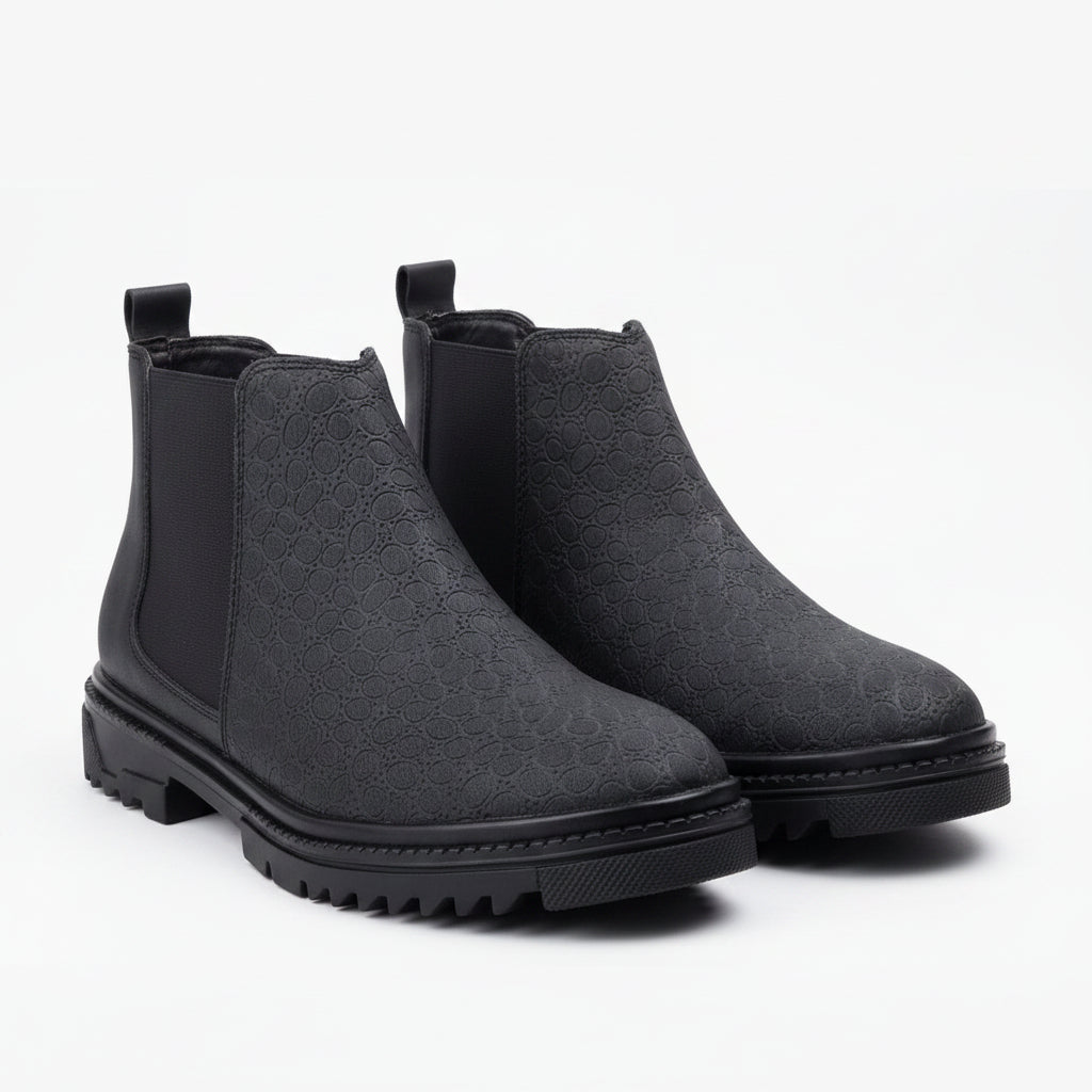 A single black Chelsea boot with a textured, embossed pattern on the upper and a black elastic side panel, shown on a clean white background.