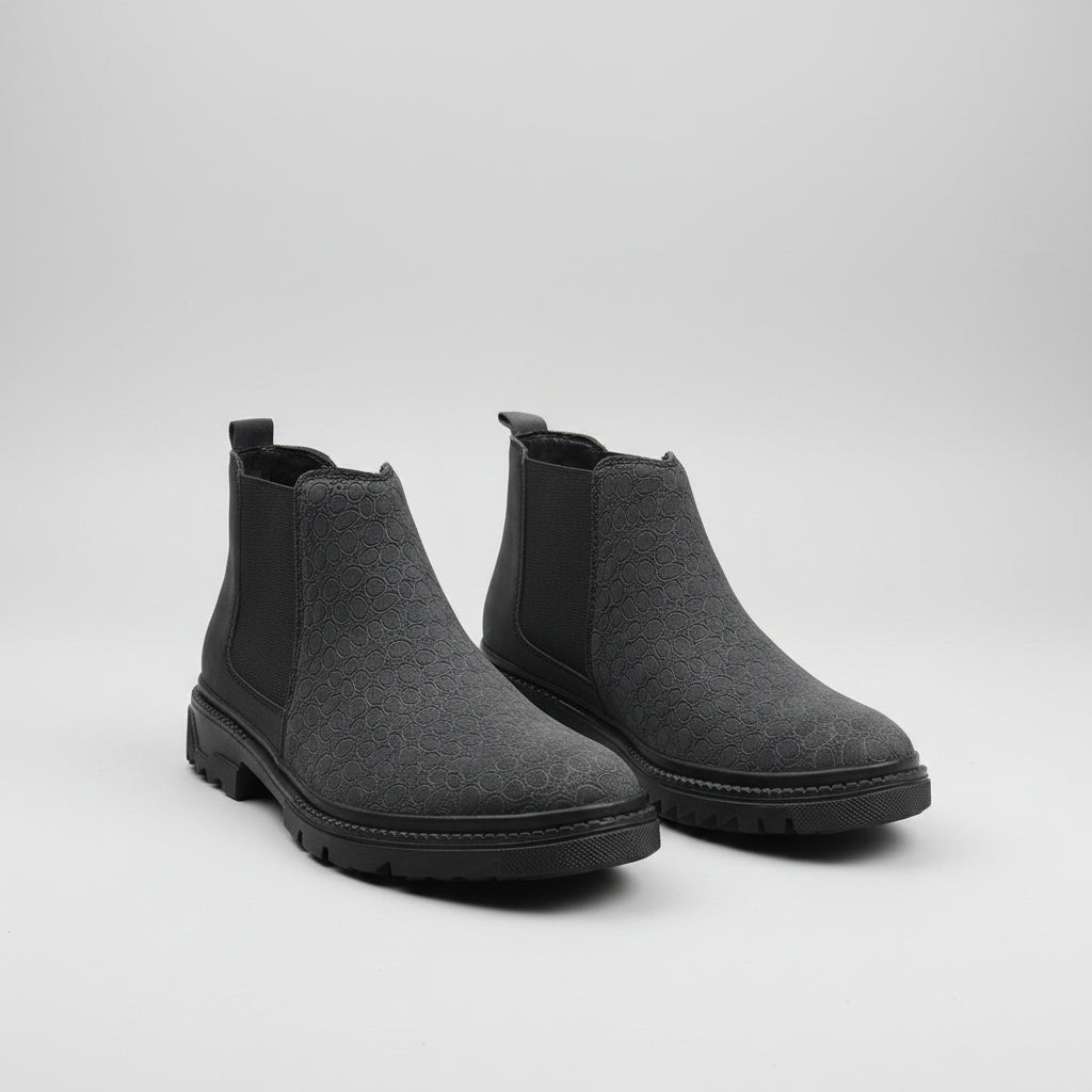 Pair of gray Chelsea boots on a textured surface with a brown curtain background
