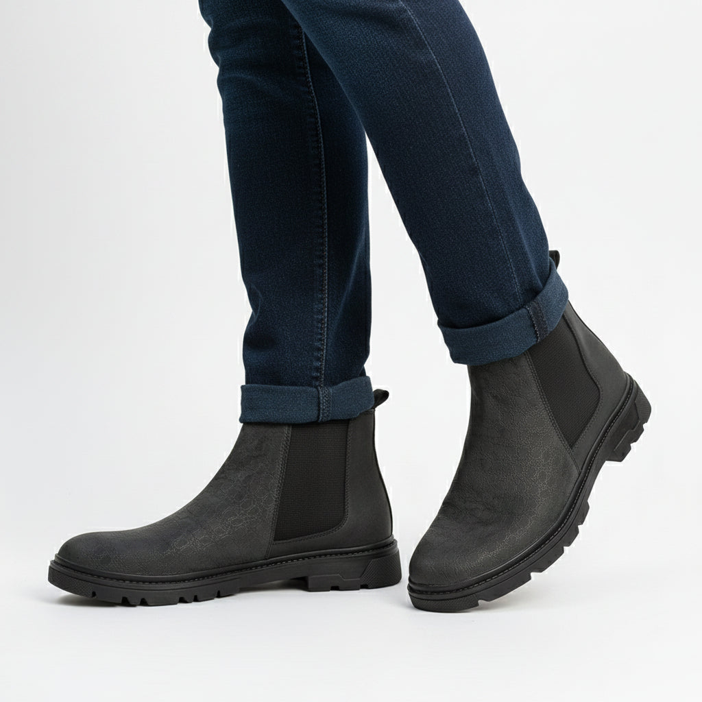 Person wearing dark gray Chelsea boots on a cobblestone street.