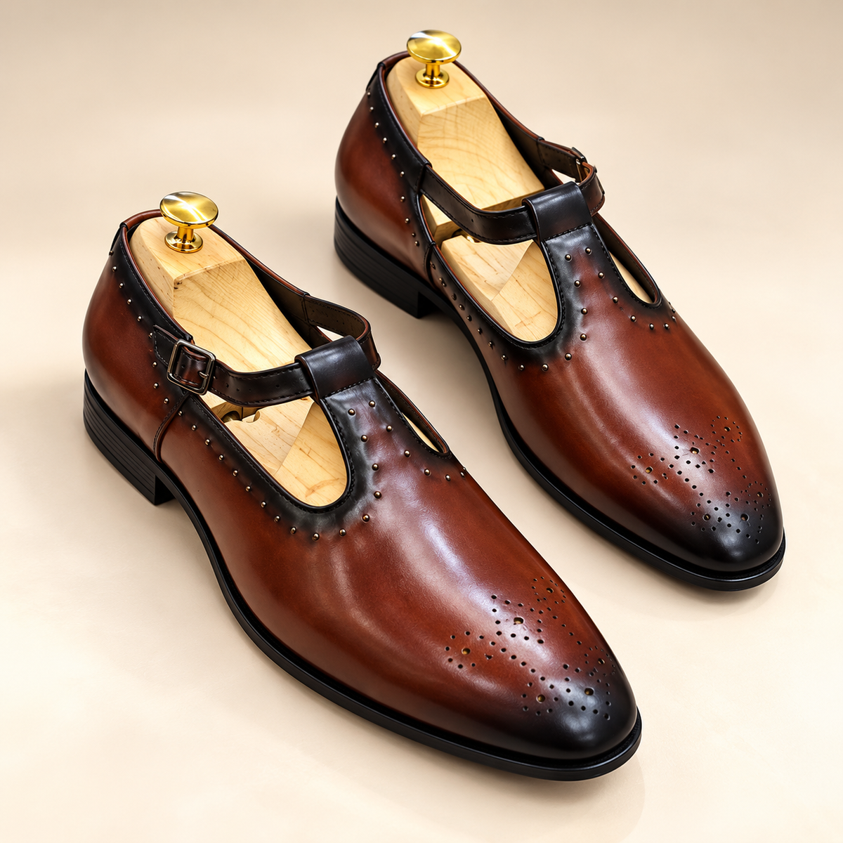 A pair of dark brown leather T-strap dress shoes with brogue perforations and black toe caps, displayed on wooden shoe trees against a light beige background.