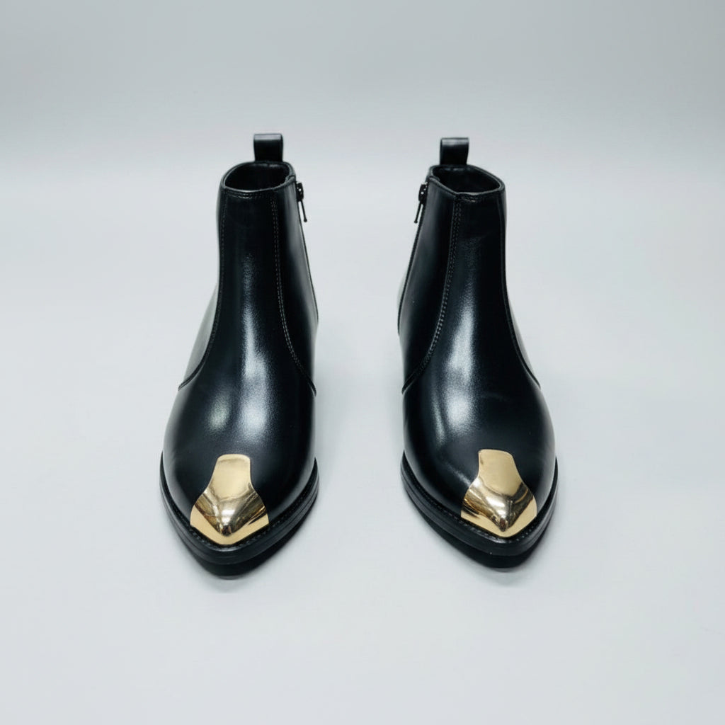 Black leather boots with gold accents held by a hand against a yellow box background