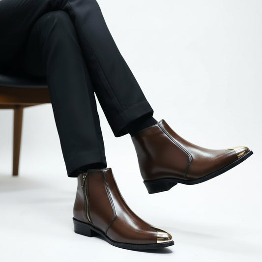 A pair of brown leather Chelsea-style ankle boots with metallic gold toe caps, held by a hand with yellow boxes in the background.