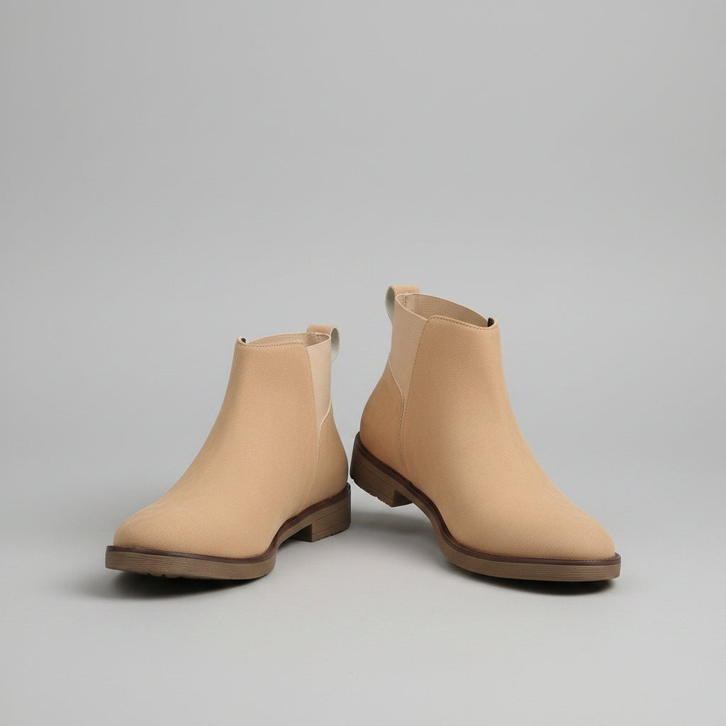 Pair of beige ankle boots on a wooden surface with a curtain in the background