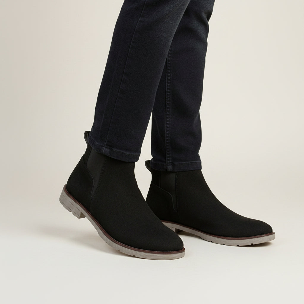 Black Chelsea boots worn with dark jeans on a stone pavement.