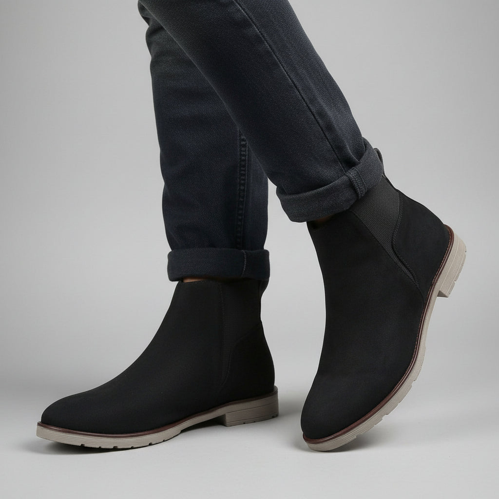 Black ankle boots worn with rolled-up jeans on a beige background